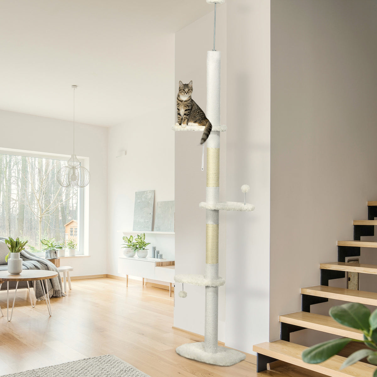 Cat on the top perch of a white floor to ceiling cat tree in a modern home with stairs